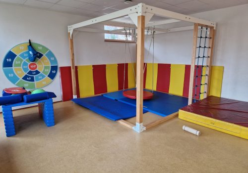 Turnraum mit Schaukelgerüst, Kletterwand, bunten Matten und Zielscheibe